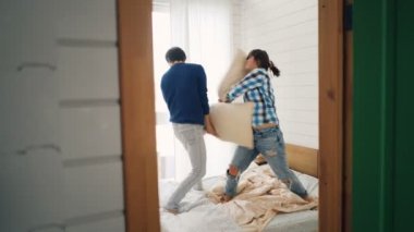 Oynak karı koca yastık savaşı ile Çift Kişilik Yatak ev gülüyor ve rahatlatıcı üzerinde eğleniyor musun. İlişki, aptal aktivite ve eğlence kavramı.