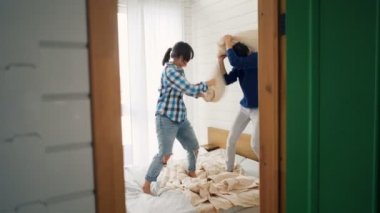 Oynak genç çift yakışıklı Asyalı adam ve güzel beyaz kız çift kişilik yatakta yastıklar tartışıyorlar, eğlenceli ve gülüyor. Modern yaşam tarzı ve ilişki konsepti.