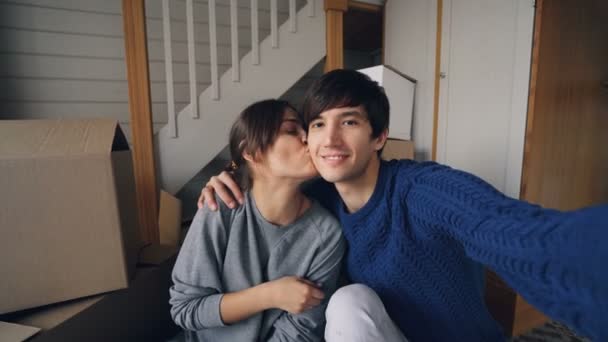 Point of view shot of good-looking man taking selfie with his pretty wife in new home kissing, hugging and showing keys and trendy hand gestures. Guy is holding camera. — Stock Video