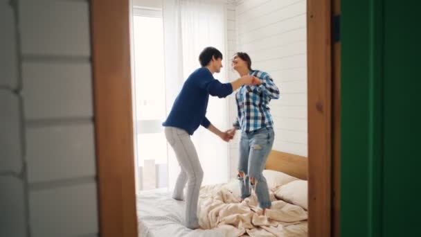 Šťastní mladí lidé tančí na posteli doma pohybující se těla a drží ruce, které si užívají lásku a volný čas spolu. Koncepce bydlení, mládí a volný čas. — Stock video