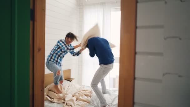 Opgewonden jonge man en vrouw zijn plezier in huis vechten kussens en lachen dan knuffelen en zoenen. Huizen, vrijetijdsactiviteiten en gehuwd leven concept. — Stockvideo