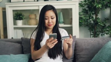Neşeli genç bayan banka kartı tutan ve smartphone ekran dokunaklı o zaman mutlu bir şekilde gülümseyerek online ödeme yapıyor. Finans, internet alışveriş ve gençlik kavramı.