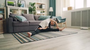 İnce Asyalı kız kız öğrencinin evde halı katta oturan ve bükme zevk germe egzersizleri yoga yapıyor. Güzel bir daire görünür.