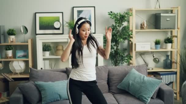 Radostné mladá žena šťastná student je posloucháte hudbu přes sluchátka a tance si užívat oblíbené skladby ve stylovém bytě. Lidé a volný čas. — Stock video