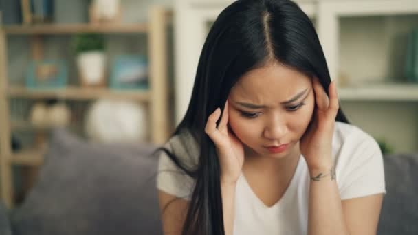 Несчастная азиатка-студентка чувствует себя плохо из-за головной боли и пытается избавиться от боли, массируя голову, касаясь висков с грустным лицом. Больной молодежный концепт . — стоковое видео