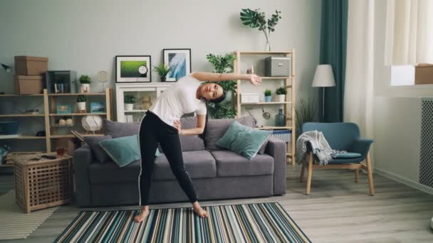 Esbelta esportista asiática está fazendo esportes em casa praticando sozinho dobrando para a direita e para a esquerda, em seguida, para a frente durante a prática pessoal. Conceito de bem-estar e juventude . — Vídeo de Stock