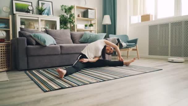 Стройная азиатка-студентка занимается йогой дома, наслаждаясь упражнениями на растяжку, сидя на полу на ковре и изгибе. Квартира видна . — стоковое видео