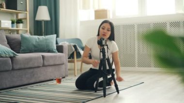 Çekici Asya blogger kamera tripod ve donatım ayarlama sonra katta oturan ve online vlog için video kayıt yüklüyor. Teknoloji ve yaşam tarzı kavramı.