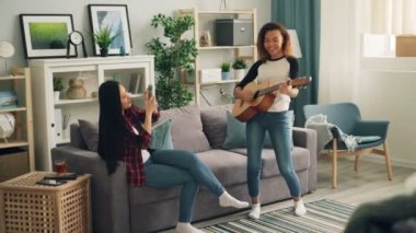 Asya arkadaşı smartphone ve müzik ve dostluk zevk gülümseyen ile video kayıt ederken şirin Afrikalı-Amerikalı kadın evde gitar çalıyor.