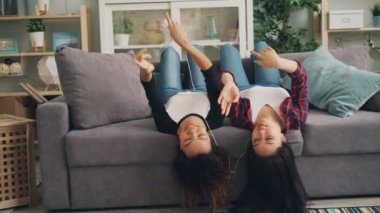 Kaygısız genç kadınlar smartphone kullanarak ve koltukta yalan ve elleri ve ayakları hareketli dans kulaklık aracılığıyla müzik dinlerken. Gençlik ve gevşeme kavramı.