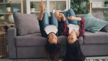 Mutlu kız arkadaş müzik dinlerken kulaklık ile smartphone kullanarak ve yalancı ters dans evde kanepe. Eğlenceli, gençlik ve Gadget'ları kavramı.