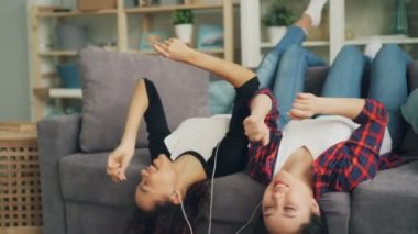 Güzel kızlar Afrika Amerika ve Asya earphones ve kanepe üzerinde baş aşağı yalan ve birlikte dans smartphone ile en sevdiğiniz müzik tadını çıkarıyor.