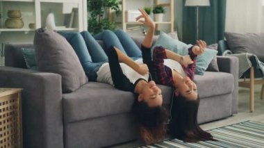 Neşeli genç bayanlar eğlenceli birlikte akıllı telefon ve kulaklık ile müzik dinlemek ve hareketli bacaklar ve eller dans evde geçiriyor. Sevinç ve dostluk kavramı.