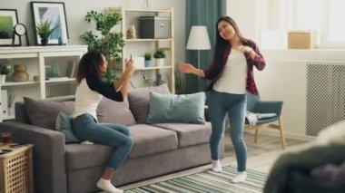 Güzel Asyalı kız casual giyim moda gömlek giymiş evde dans ediyor ve Afro-Amerikan arkadaşı ise kot video yapmak için smartphone kullanarak.