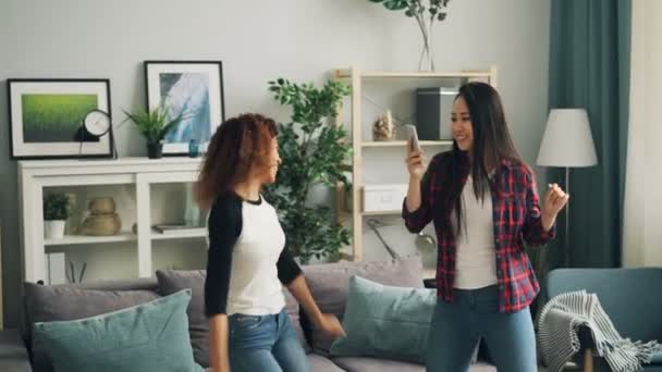 Sorglösa vänner asiatiska och afrikanska amerikanska är dans hemma party och videoinspelning med smartphone poserar för kameran och rörliga händer och kropp. — Stockvideo