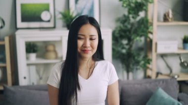 Gülümseyen ve kameraya bakarak çekici Asyalı kız beyaz T-shirt ayakta modern ev içinde ağır çekim portre. Güzel iç mekanlar ve gençlik genel kavram.