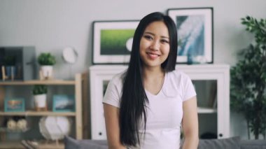 Gülümseyen ve kameraya bakarak güzel Asyalı kadın uzun saçlı modern daire içinde ayakta ağır çekim portre. Çekici insanlar ve gençlik kavramı.