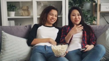 Afrika Amerika ve Asya genç bayanlar TV komedi evde, gülüyor, söz ve kanepede rahatlatıcı patlamış mısır yemek tadını çıkarıyor. Eğlence ve gıda kavramı.