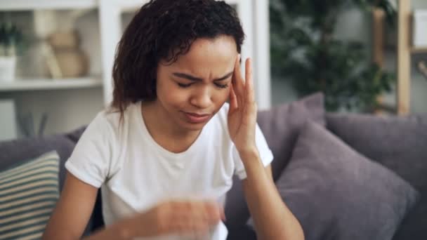 Aantrekkelijke African American girl lijdt hoofdpijn aanraken haar hoofd masseren tempels binnenshuis om thuis te zitten. Pijn, jeugd en gezondheid concept. — Stockvideo
