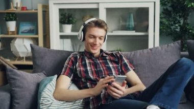 Yakışıklı genç hippi müzik aracılığıyla, ekran dokunaklı ve gülerek smartphone kullanarak dinliyor. Modern teknoloji ve eğlence kavramı.