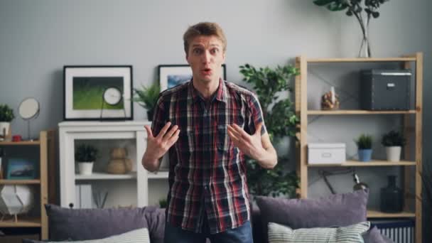 Retrato de un joven enojado gritando y haciendo gestos expresando fuertes emociones negativas de pie en la casa moderna y mirando a la cámara y luego alejándose . — Vídeos de Stock