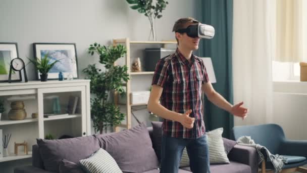 Excited guy is having fun with virtual reality goggles wearing headset and moving arms standing in room at home alone and smiling. Youth lifestyle and devices concept. — Stock Video