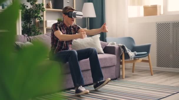 Vzrušený chlap se baví s rozšířená realita brýle nosit sluchátka a hrát závodní hra pohybující se ruce a nohy vyjadřují pozitivní emoce. — Stock video