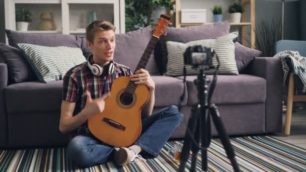 专业音乐家博主正在录制有关使用相机为互联网博客弹吉他的教程。他正在和追随者交谈, 他们展示乐器, 然后演奏. — 图库视频影像
