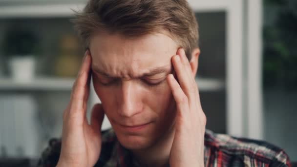 Close-up shot van ongezonde jongen zijn hoofd aan te raken vanwege migraine masseren tempels binnenshuis. Zieke jongeren, niet goed voelt en physican ziekte concept. — Stockvideo