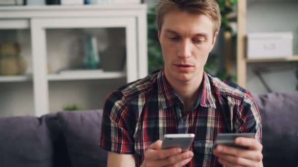 Веселый молодой человек делает онлайн-платеж с банковской картой касаясь экрана смартфона, а затем счастливо улыбается. Финансы, интернет-магазины и молодежная концепция . — стоковое видео