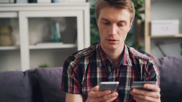 Joven alegre está haciendo el pago en línea con tarjeta bancaria tocando la pantalla del teléfono inteligente y luego sonriendo felizmente. Finanzas, compras por Internet y concepto juvenil . — Vídeo de stock