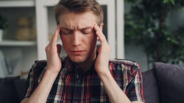 Ongelukkige ziek jonge man lijdt aan ernstige hoofdpijn aan zijn hoofd masseren tempels binnenshuis thuis te raken. Pijn, moe jeugd en slechte gezondheid concept. — Stockvideo