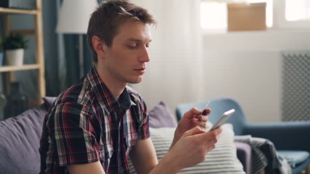 Hombre guapo está haciendo el pago electrónico con tarjeta de crédito y teléfono inteligente que toca la pantalla y luego sonríe disfrutando de la tecnología moderna. Millennials y concepto bancario . — Vídeo de stock