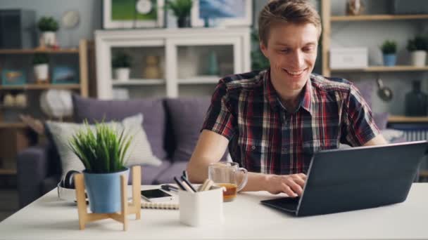 快乐的自雇人士是在家里工作使用笔记本电脑笑着笑着享受他的成就。现代技术、青年和工作理念. — 图库视频影像