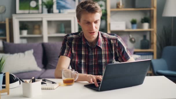 Sikeres férfi szabadúszóként dolgozik otthon ülő-on iskolapad stúdióban képernyő gépelés, és mosolyogva néztem laptop. Üzleti- és ifjúsági koncepció. — Stock videók