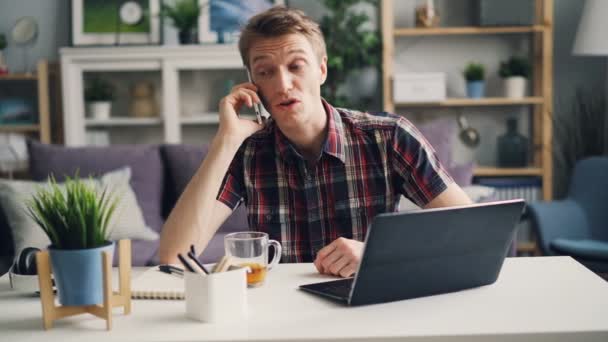 快乐的家伙正在用手机交谈, 并使用笔记本电脑在家里做遥远的工作。现代技术、通信和职业理念. — 图库视频影像