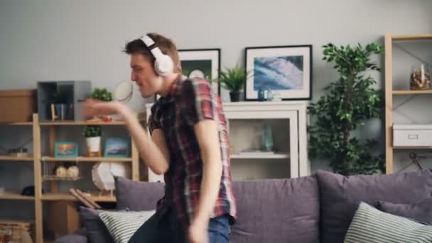 Emocional hombre melómano está escuchando música rock a través de auriculares bailando y cantando en piso moderno divirtiéndose. Gente, tecnología moderna y concepto de estilo de vida . — Vídeo de stock