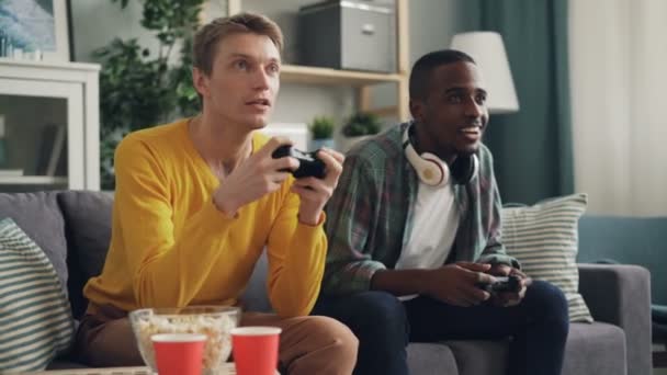 Afroamericanos y caucásicos están jugando videojuegos y luego haciendo chocar los cinco y darse la mano. Tecnología moderna, entretenimiento y concepto de apartamento . — Vídeo de stock