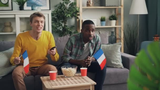 Los jóvenes fanáticos del deporte francés están apoyando al equipo favorito viendo el partido en la televisión y ondeando banderas de Francia y luego haciendo chocar los cinco. Patriotas, animar y concepto de casa . — Vídeo de stock