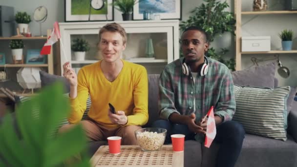 Bonitos rapazes fãs de esportes estão assistindo competição na TV segurando bandeiras canadenses, em seguida, celebrando a vitória se divertindo. Juventude, amizade e conceito de casa . — Vídeo de Stock