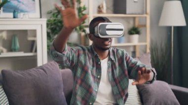 Afrikalı-Amerikalı genç adam kulaklık giyen evde yalnız eğleniyor artar gerçeklik bardaklarda oyun oynuyor. Millennials ve Gadget'ları kavramı.