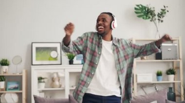 Neşeli Afrikalı-Amerikalı adam dans ve modern daire boş zaman evde zevk kulaklık ile müzik gülüyor. Eğlence ve Gadget'ları kavramı.