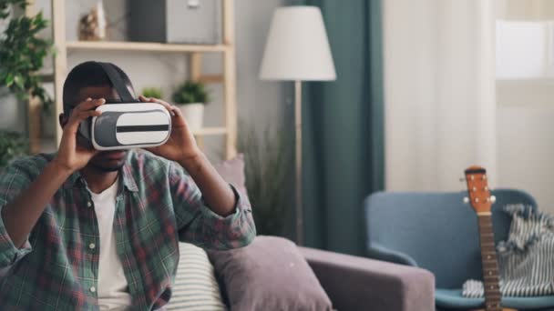 Афроамериканский студент развлекается в очках виртуальной реальности, надевая устройство и двигая руками, расслабляясь дома, наслаждаясь современными технологиями и отдыхом . — стоковое видео