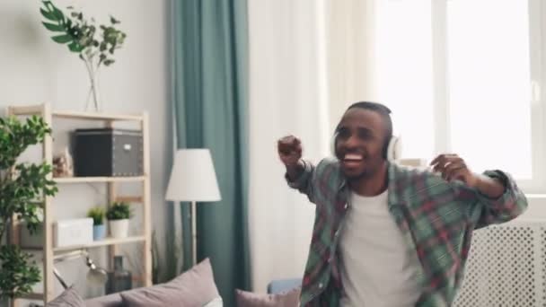 Happy man African American danseur s'amuse à la maison en écoutant de la musique dans les écouteurs et en dansant applaudissements mains. Style de vie des jeunes et concept des milléniaux . — Video