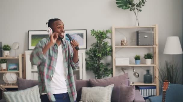 African American mężczyznom w słuchawkach jest słuchanie muzyki, taniec i śpiew w pilota zdalnego sterowania w mieszkaniu korzystających z wolnego czasu i wolność. — Wideo stockowe