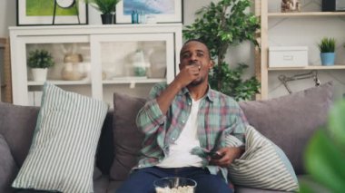 Neşeli Afro-Amerikan öğrenci komik komedi TV izlemek ve kanepede rahatlatıcı ve Uzaktan kumanda ile gülüyor. Televizyon, gençlik ve olumlu duygular kavramı.