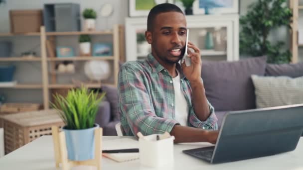 Молодих афро-американських спеціаліст розмовляє з бізнес-контакти на мобільному телефоні, сміючись і працювати з ноутбуком, насолоджуючись роботи. Концепція молоді і спосіб життя. — стокове відео