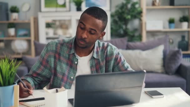 疲惫的非洲裔美国自由职业者正在与笔记本电脑和书面写作, 然后感到头痛按摩他的太阳穴触摸头。压力和千禧年概念. — 图库视频影像