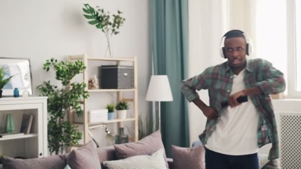 Verspielter afrikanisch-amerikanischer Mensch hat Spaß zu Hause, singt in der Fernbedienung und tanzt entspannt in einer schönen hellen Wohnung. Jugend-, Lebens- und Kulturkonzept. — Stockvideo