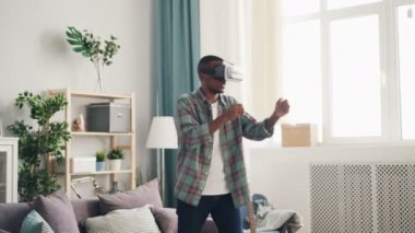 Heyecanlı genç adam sanal gerçeklik gözlüklü evde oyun oynuyor hareketli kol ve vücut duran oda ışık. Eğlenceli, modern teknoloji ve insan kavramı.